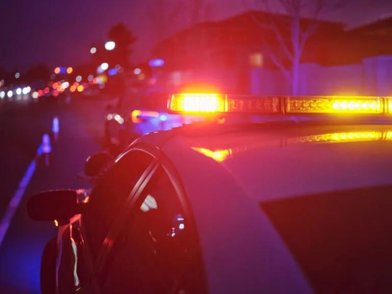 A police car at night alongside a road with emergency lights flashing.